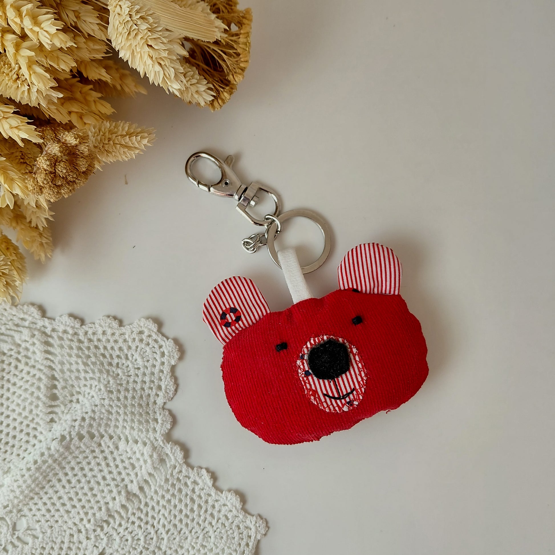 Red bear-shaped keychain with striped ears on a light surface with decorative elements.