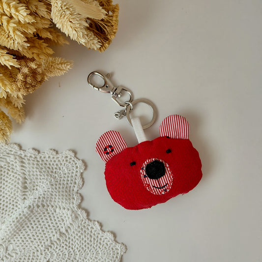Red bear-shaped keychain with striped ears on a light surface with decorative elements.