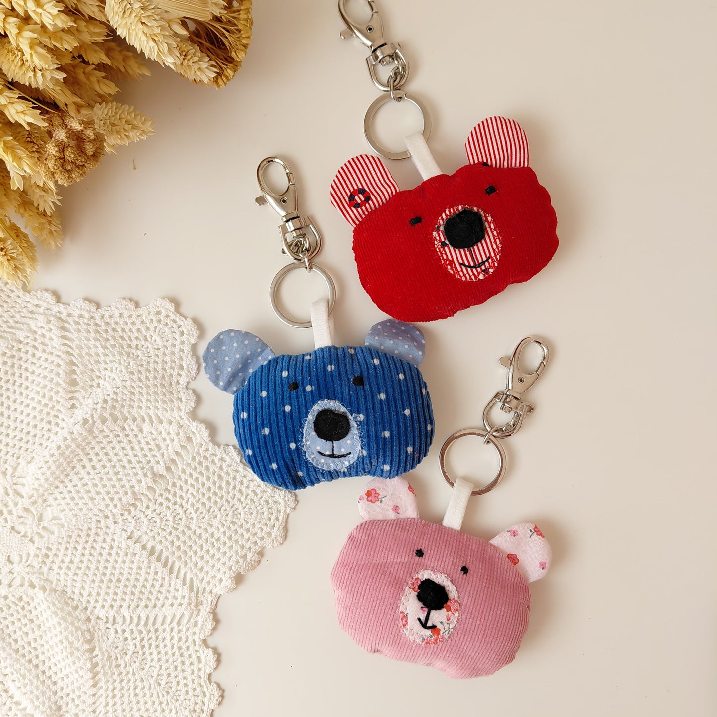 Three bear-shaped keychains in red, blue, and pink on a textured surface 