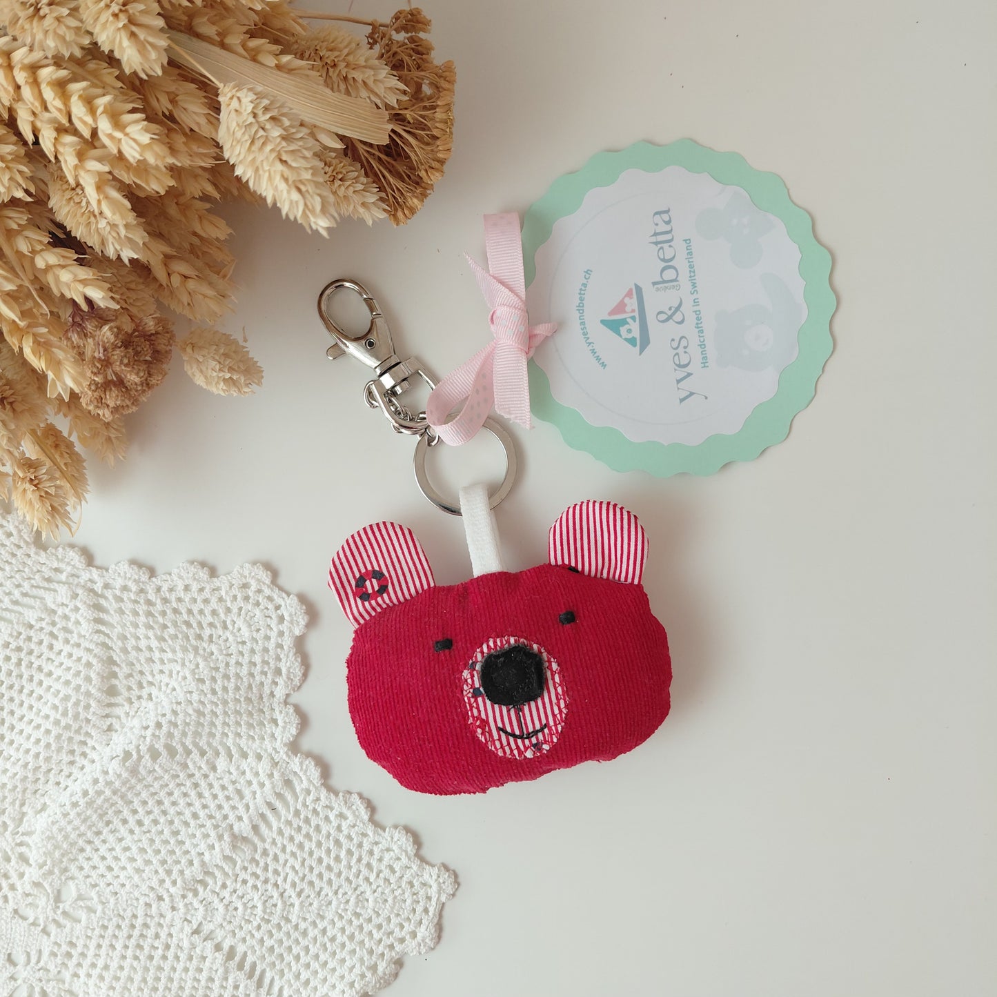 Red bear-shaped keychain with a white strap on a light surface with decorative elements.