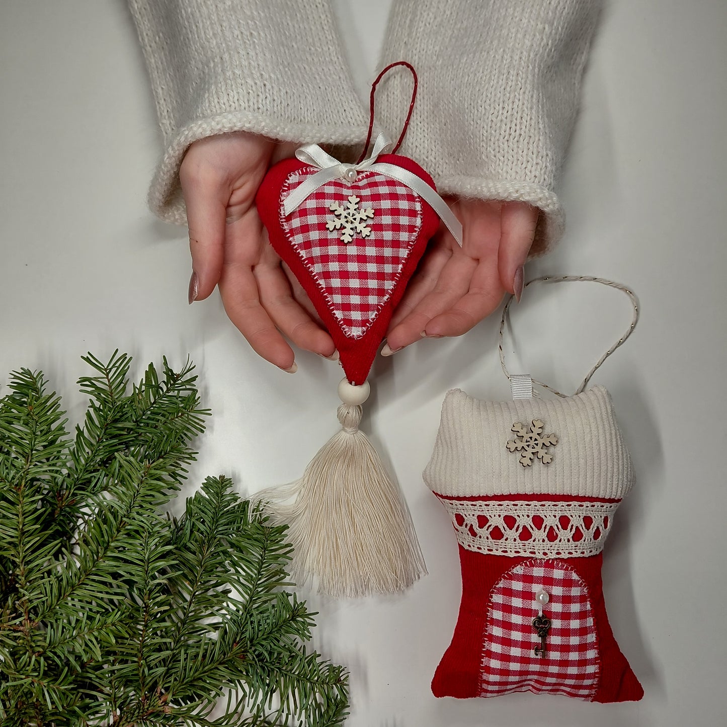 Heart-shaped red and white ornament with tassel held by a person, next to another similar ornament 