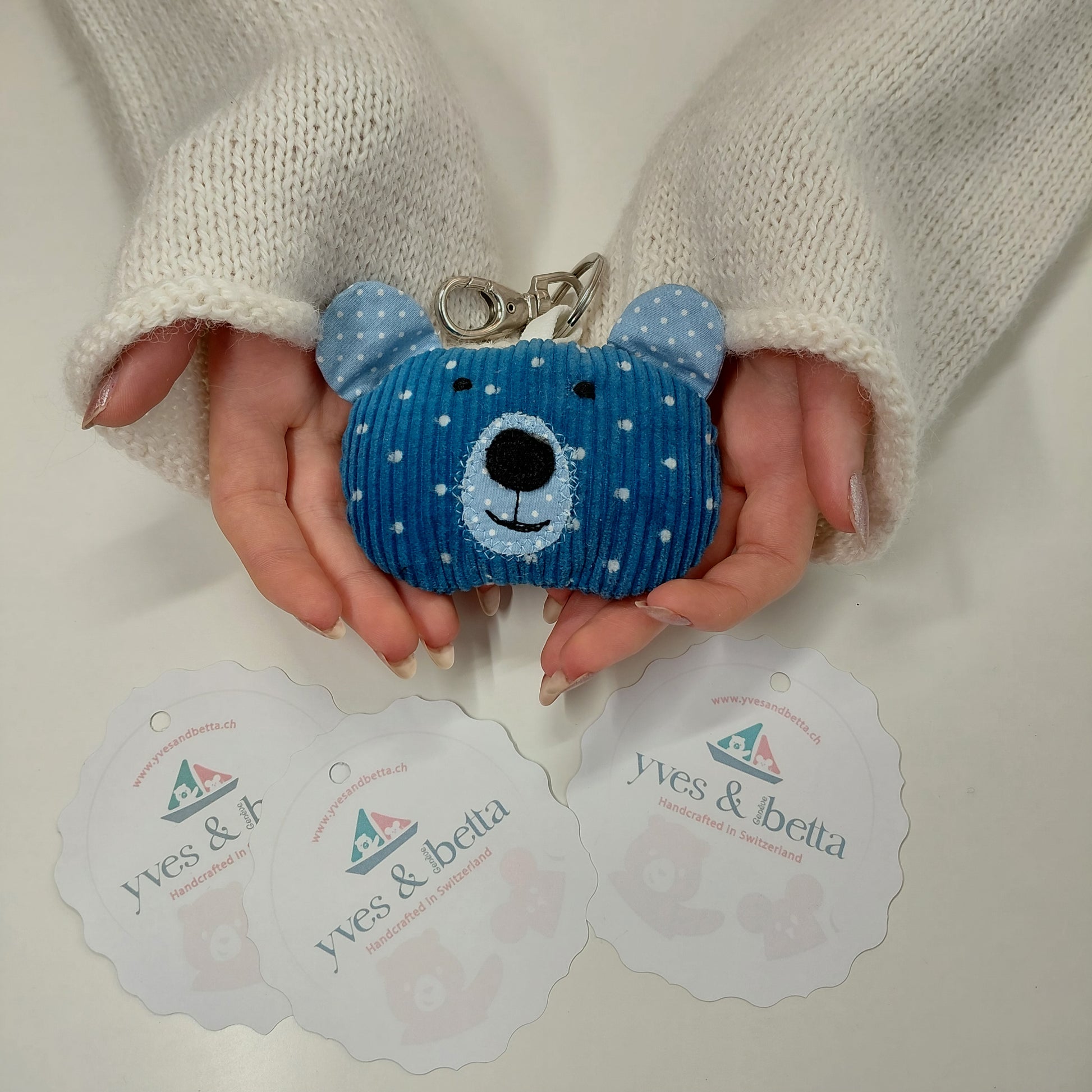 Blue bear-shaped keychain held by a person with branded cards in the background