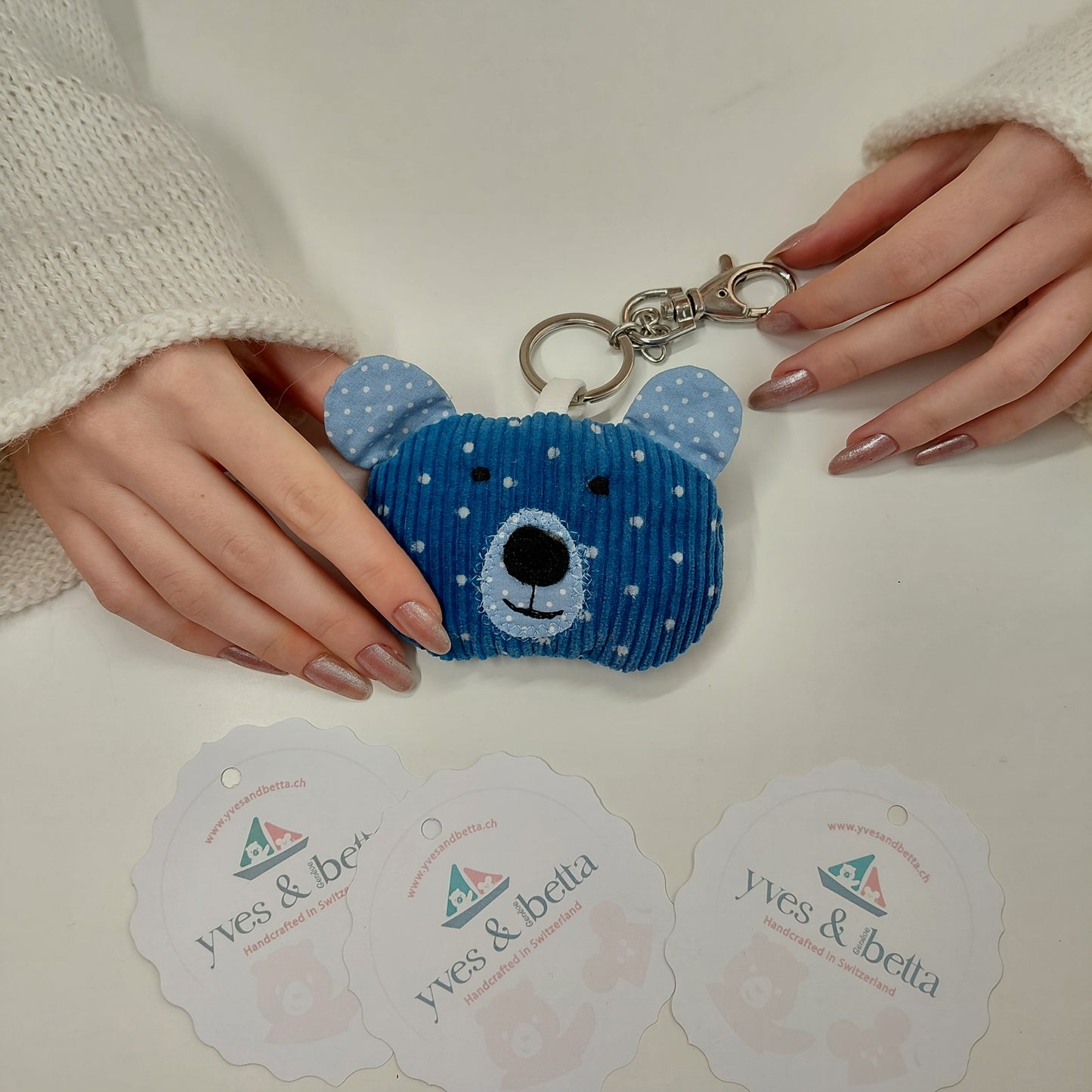 Blue bear-shaped keychain held by a person with visible brand cards in the background