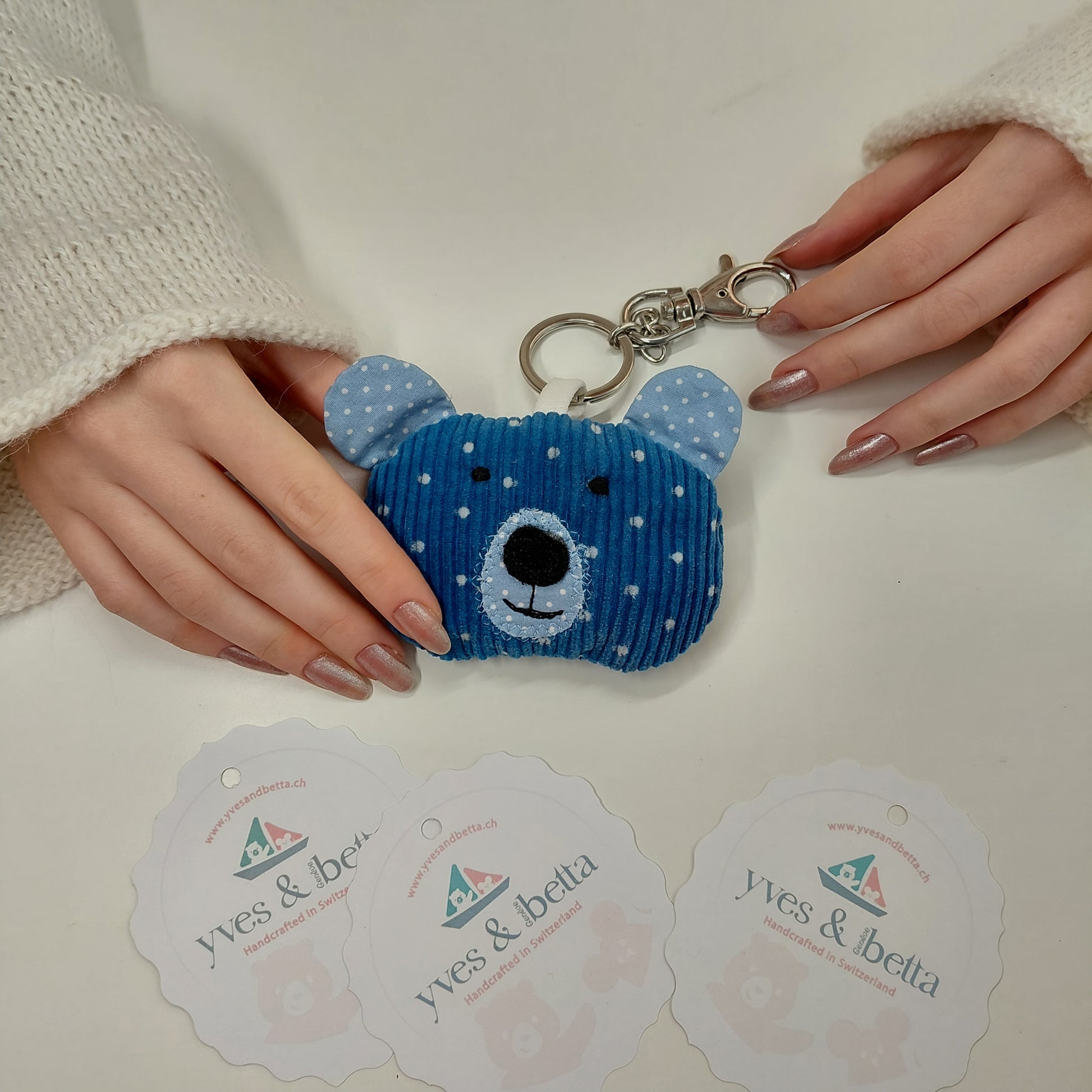Blue bear-shaped keychain held by a person with visible brand cards in the background