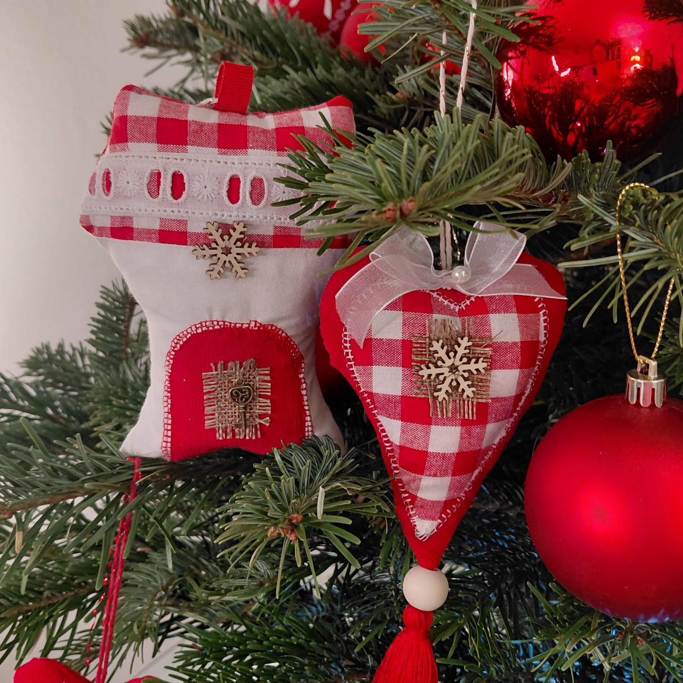 Red and white checkered heart-shaped ornaments on a Christmas tree with red balls.
